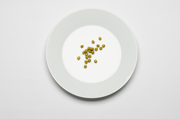 green peas lying on a white plate on a white table top view