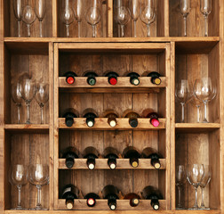 Shelving with wine bottles with glasses on wooden wall background