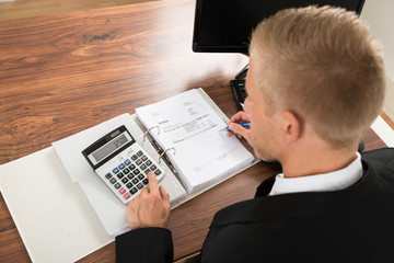Fototapeta na wymiar Businessman Calculating Invoice At Desk In Office