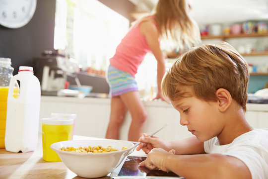 Children Eating Breakfast And Playing With Digital Tablet