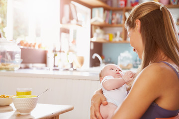 Obraz na płótnie Canvas Mother Holding Newborn Baby Daughter At Kitchen Table
