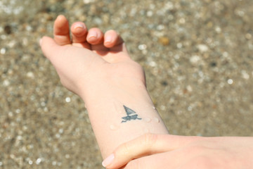 Close up of hand of young woman with ship tattooed in it, on sea background