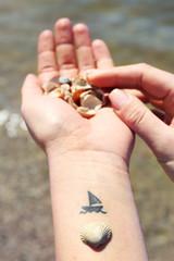 Close up of hands of young woman with ship tattooed in it, on sea background