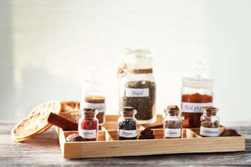 Assortment of spices in glass bottles in box, on light background