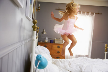 Girl In Ballerina Outfit Jumping On Parents Bed © Monkey Business