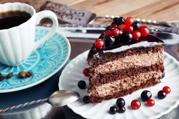 Delicious chocolate cake with berries and cup of coffee on table close up