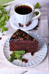 Delicious chocolate cake with mint and cup of coffee on table close up
