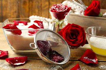 Making candied rose flower petals with egg whites and sugar, on wooden background