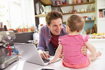 Father With Young Daughter Using Laptop In Kitchen