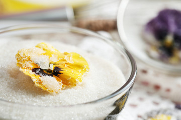 Candied sugared violet flowers, in glass bowl with sugar, on wooden background