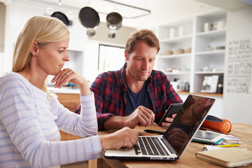 Stressed couple sitting in their kitchen using computers