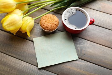 Cup of coffee with fresh cupcake, tulips and blank sheet of paper on wooden background