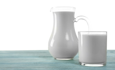 Pitcher and glass of milk on wooden table, on white background