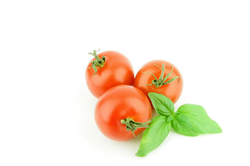 three fresh ripe tomatoes with some basil leaves on a white background.