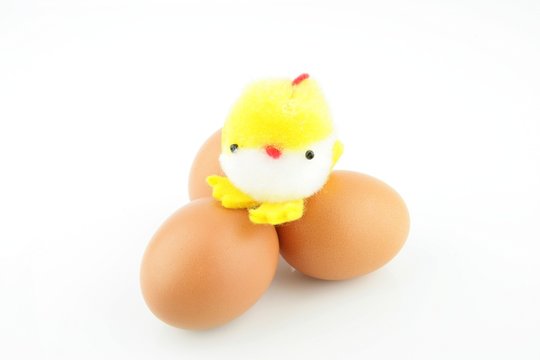 Little yellow stuffed easter chick on top of three eggs, on a white background.