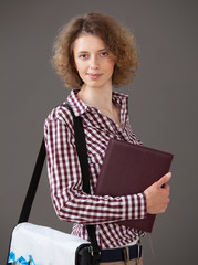 Portrait of a young woman holding a book and a briefcase