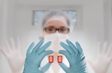 Two hands in gloves hold two liquid samples in front of a tech - obrazy, fototapety, plakaty