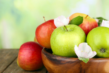 Fresh apples with apple blossom in bowl, on wooden table, on nature background