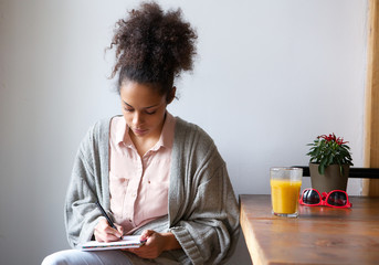 Young woman sitting at home writing on note pad © mimagephotos