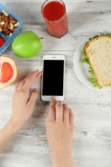 Food and mobile phone in female hands on wooden background