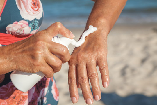 Elderly woman in swimsuit using cream for hand on beach