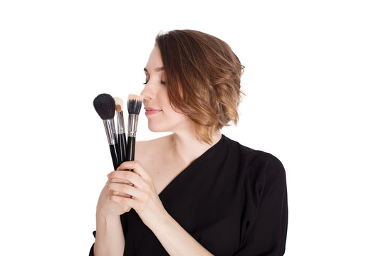 Portrait of the beautiful woman with make-up brushes near attractive face. Adult girl posing over white background