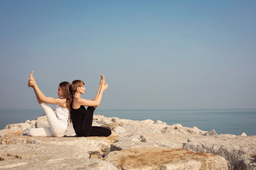 Beautiful stretch  girls practicing yoga fitness on the beach on the rocks, Krounchasana yoga posture