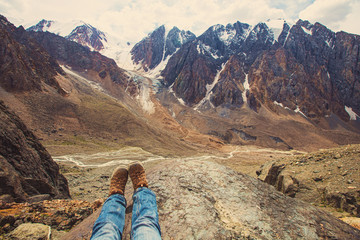 Legs of traveler sitting on a high mountain top in travel. Freedom concept