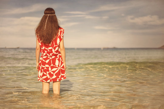 Young pretty woman in red dress standing and thinking on the sea