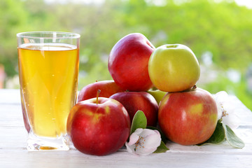 Glass of apple juice and apples on wooden table, on nature background