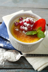 Creme brulee dessert with fresh strawberry berries on napkin, on color wooden background