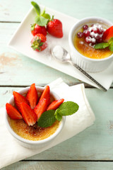 Creme brulee dessert with fresh strawberry berries on napkin, on color wooden background