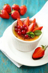 Creme brulee dessert with fresh strawberries and mint leaves, on color wooden background
