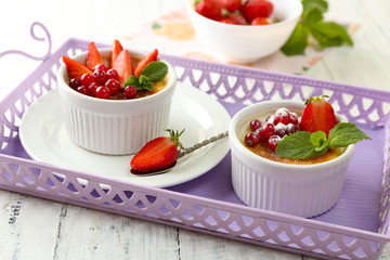 Creme brulee dessert with fresh strawberries and mint leaves, on color wooden background