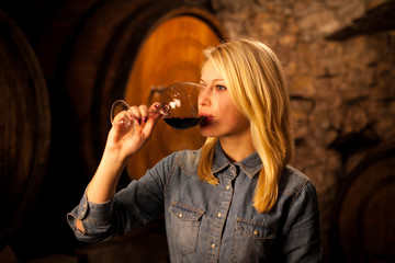 Beautiful young blond woman tasting red wine in a wine cellar - obrazy, fototapety, plakaty