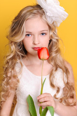 Beautiful blonde girl holding red tulip over yellow