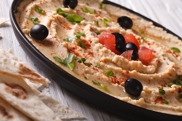hummus with olives and tomatoes on a plate close-up. 
