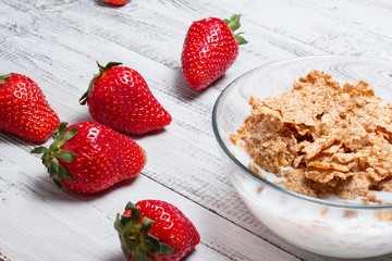 Milk, cereal and strawberries on a wooden table.