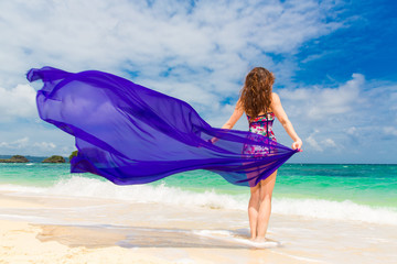 Happy young brunette in a swimsuit dancing with a purple cloth 