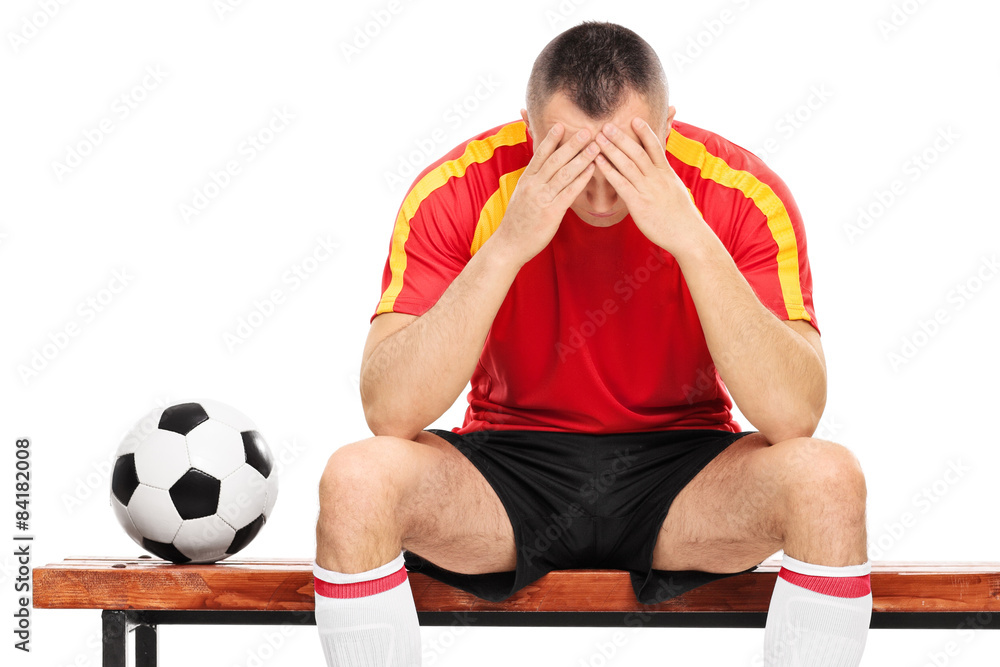 Wall mural Worried young football player sitting on a wooden bench isolated