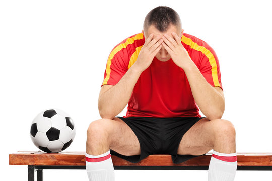 Worried young football player sitting on a wooden bench isolated