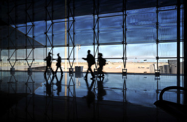 travellers walk silhouetted through an airport terminal 