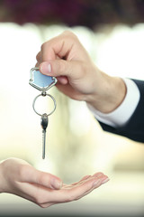 Hand of businessman giving keys to female hand on blurred background