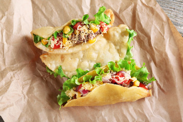 Tasty taco with vegetables on paper close up