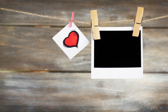 Bright heart and photo paper hanging on rope on wooden background