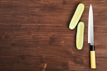 Halves of cucumber with knife on wooden background