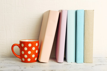 Fototapeta na wymiar Books and cup on wooden shelf on wallpaper background