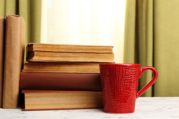 Books and cup on wooden table, on curtains background