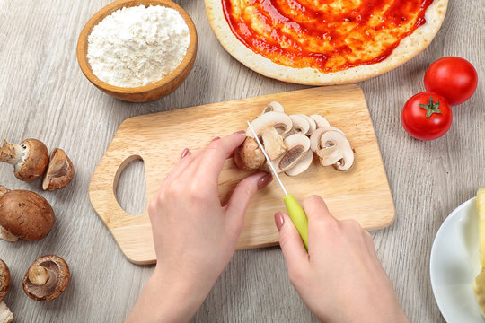 Female hands cooking pizza on wooden table, closeup