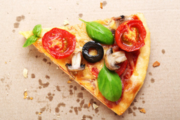 Slice of tasty pizza with vegetables and basil in cardboard box close up
